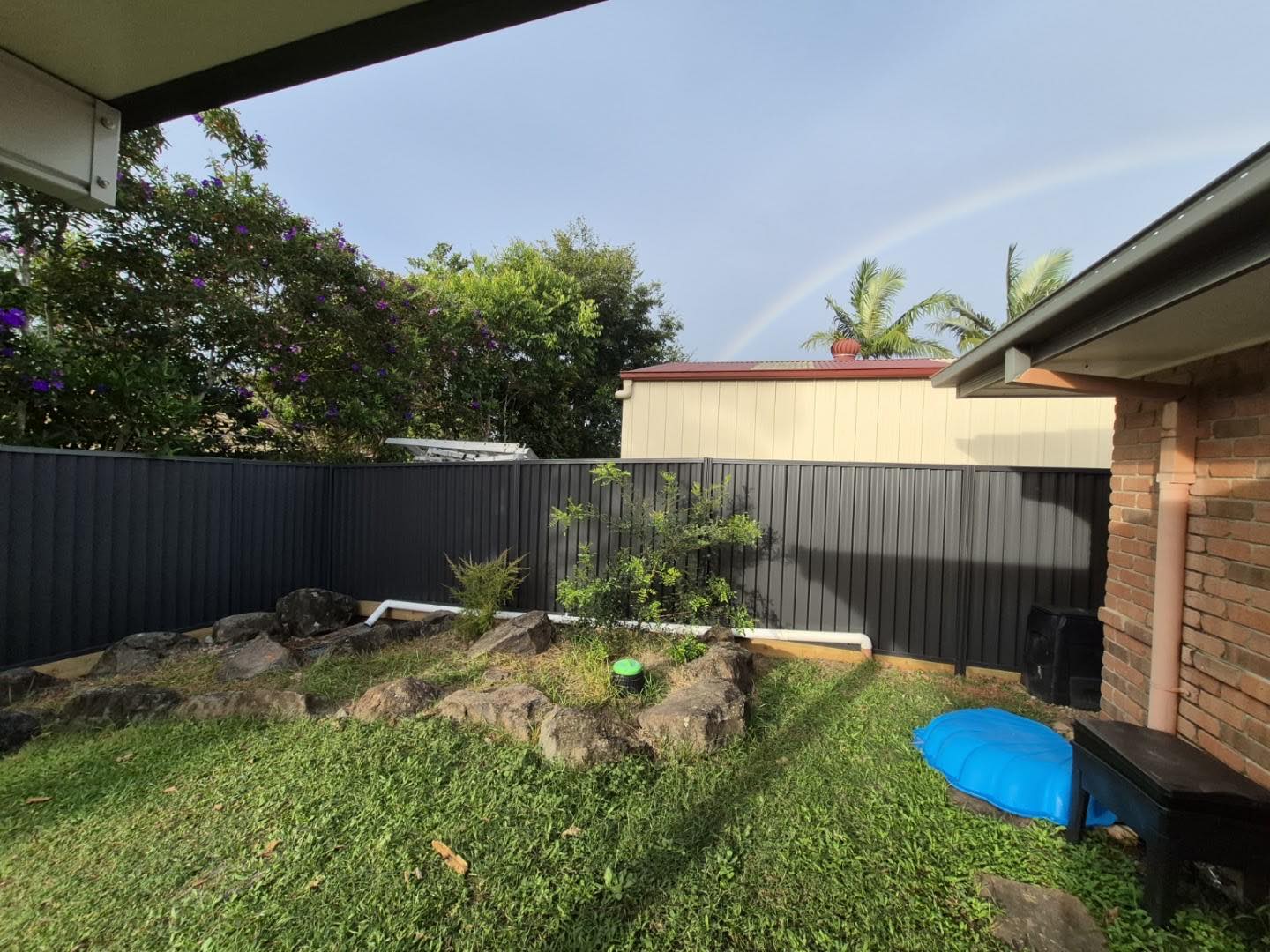 A Colorbond fence enclosing a back garden with a small pool and planting