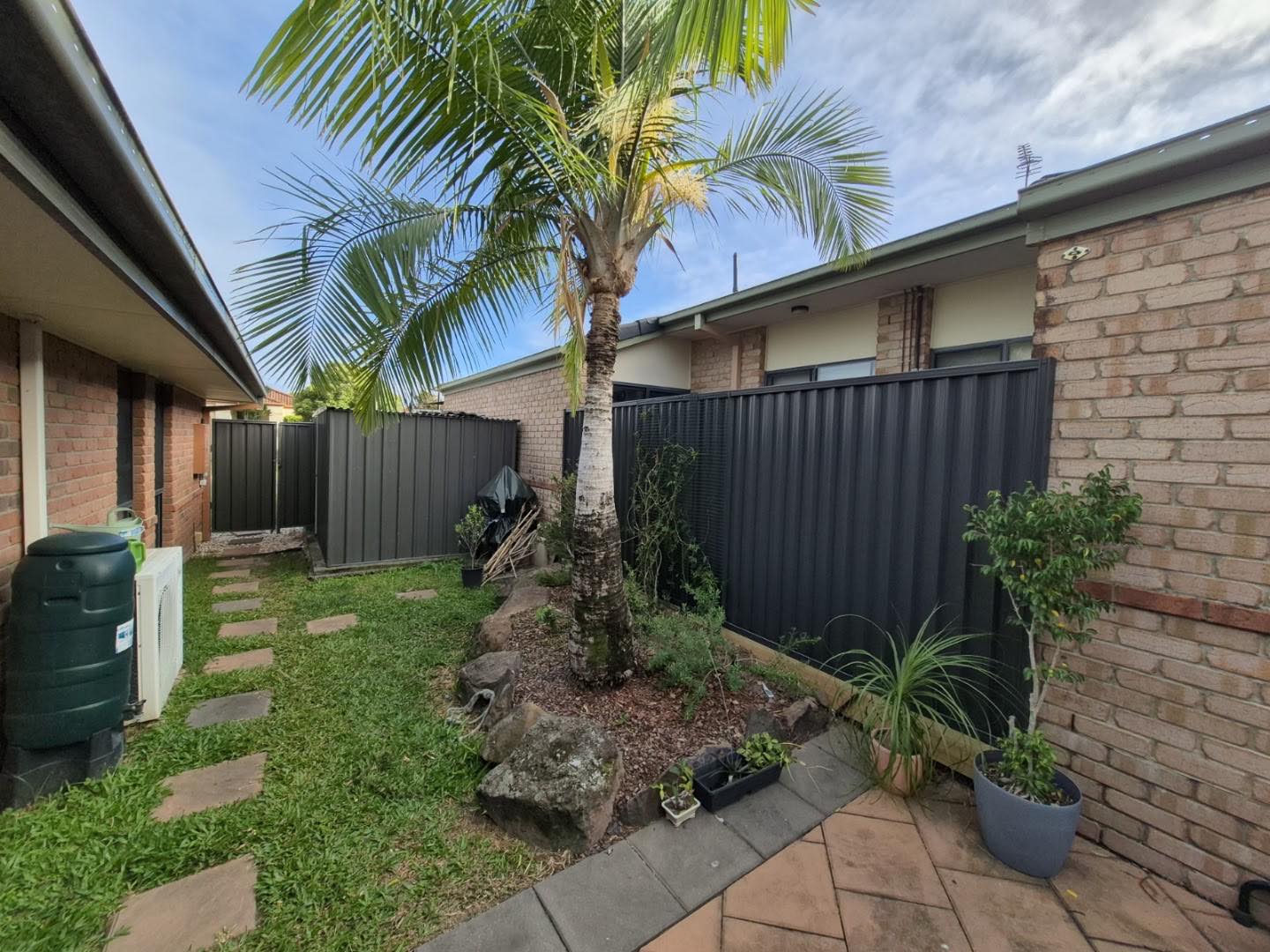 A charcoal Colorbond fence beside a palm and a paved garden path