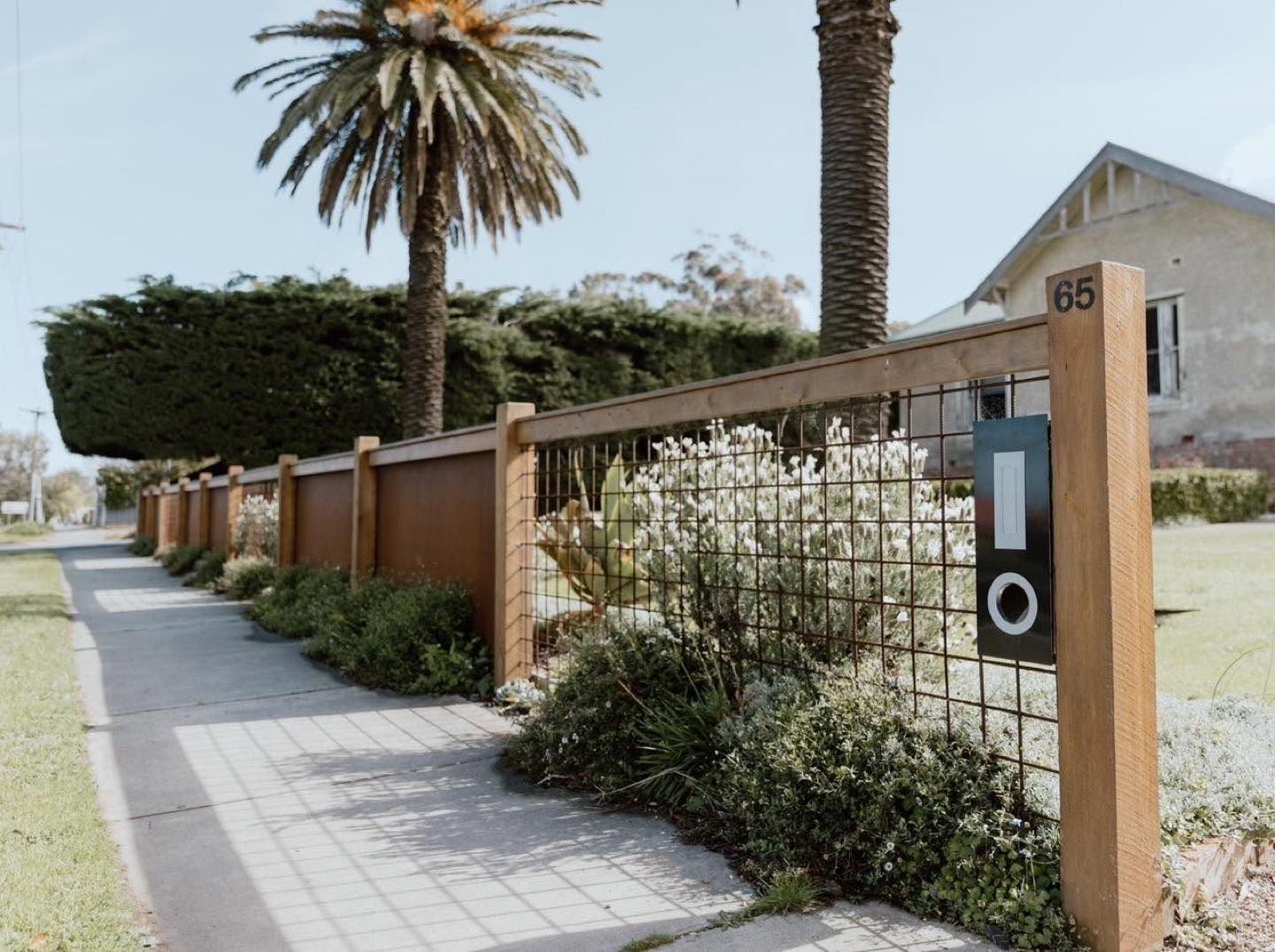 A timber-framed feature fence beside a footpath with tall palms behind it
