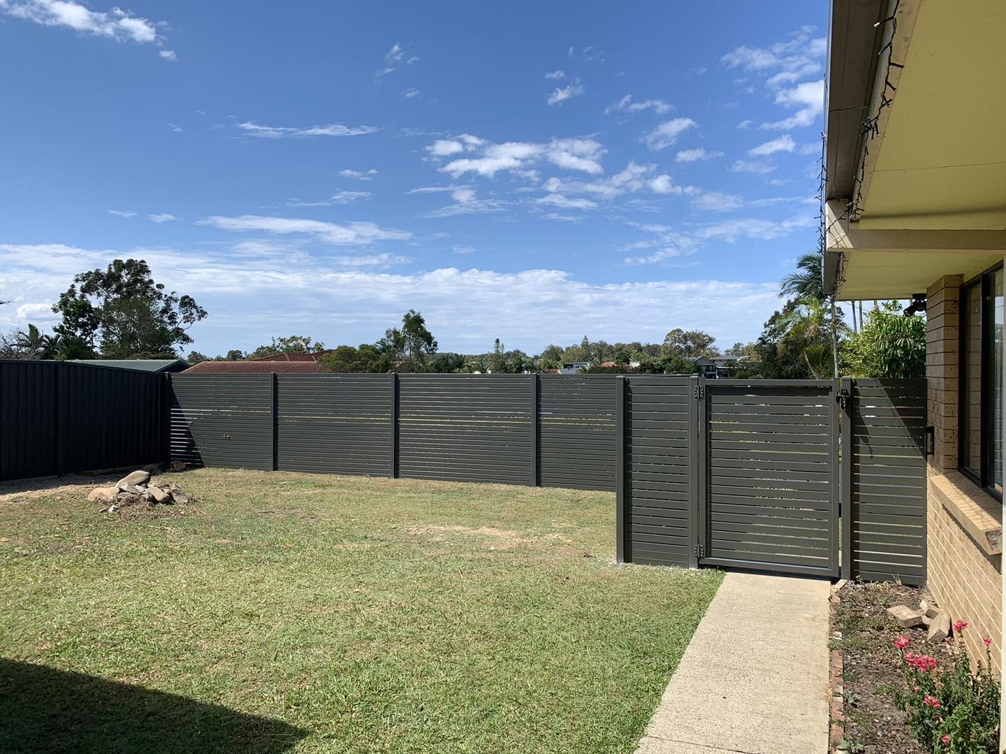 A grey Colorbond boundary fence around a level back lawn under a clear sky