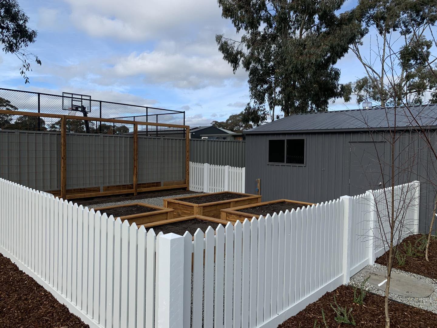 A white picket fence around a yard with a timber deck frame behind it