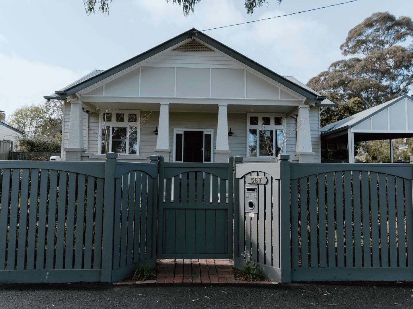 A dark green timber picket fence and matching gate in front of a weatherboard cottage