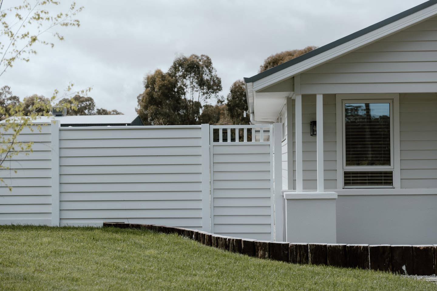 A white slatted privacy fence in front of a modern weatherboard home