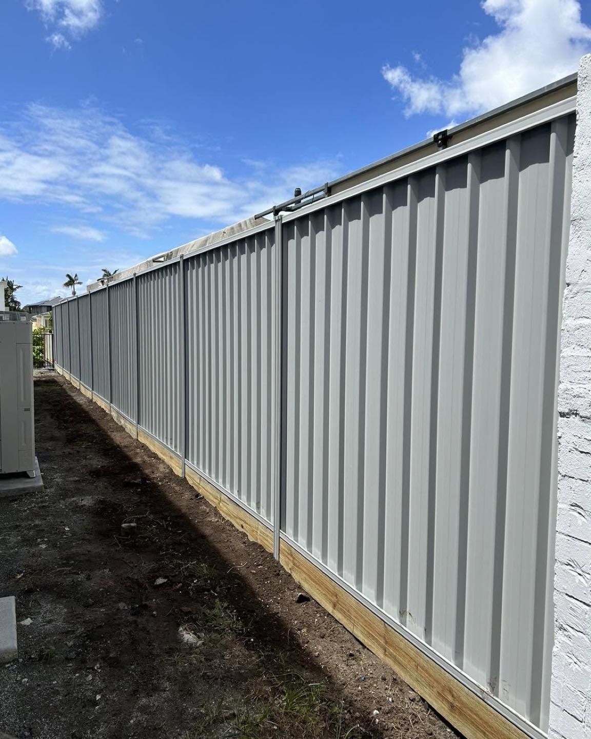 A new Colorbond fence running away down a boundary with palms behind it