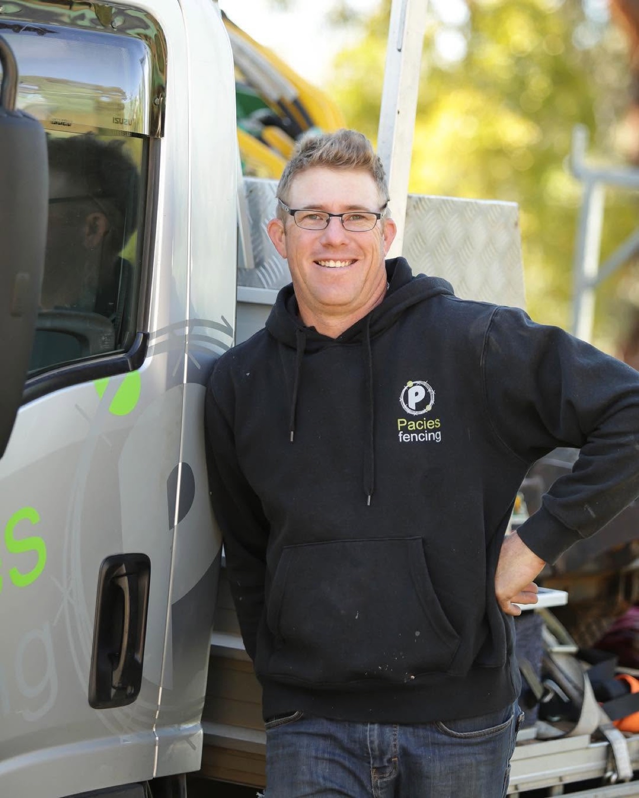 Simon standing beside the Pacies Fencing truck in a branded Pacies hoodie