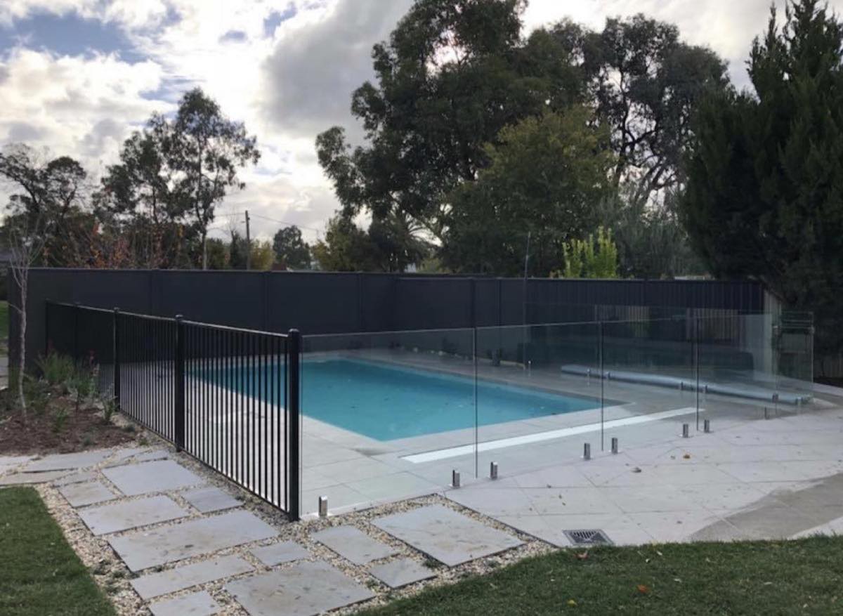 A frameless glass pool fence around a paved pool surround