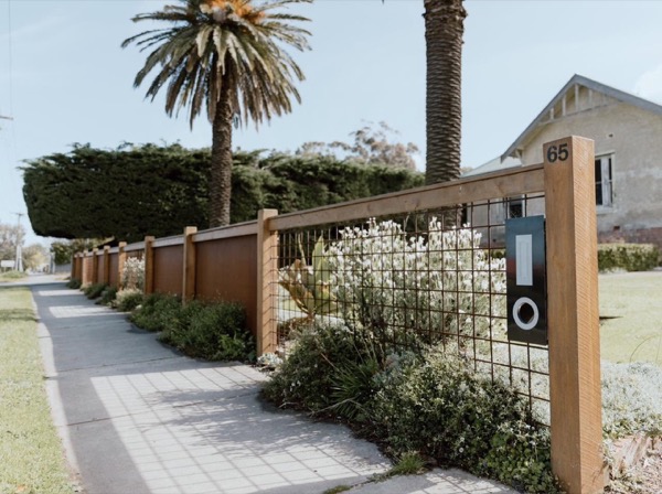 A timber-framed feature fence along a footpath with tall palms behind it