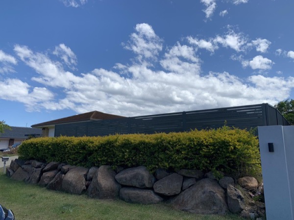 A dark Colorbond fence behind a rock retaining wall and a clipped hedge