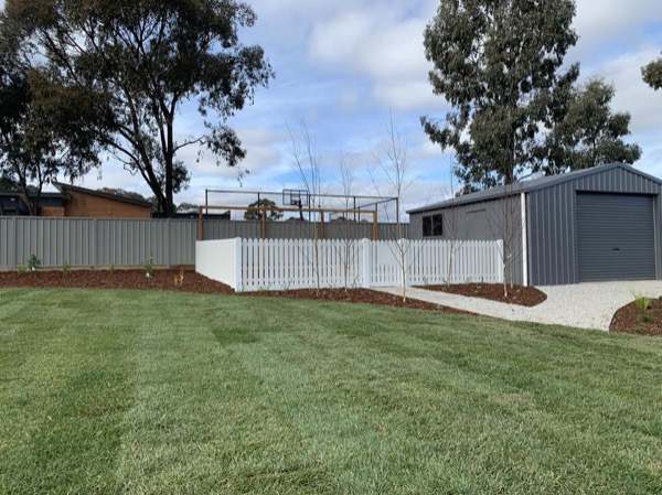 A dark grey Colorbond fence running along the back of a lawn beside a shed