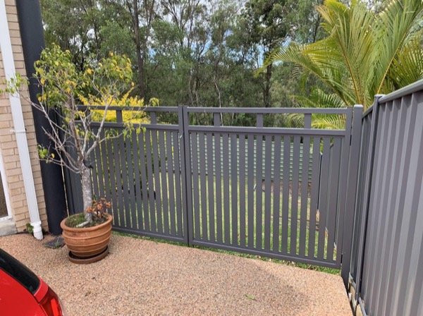 A Colorbond fence turning a corner beside a paved courtyard and potted plants