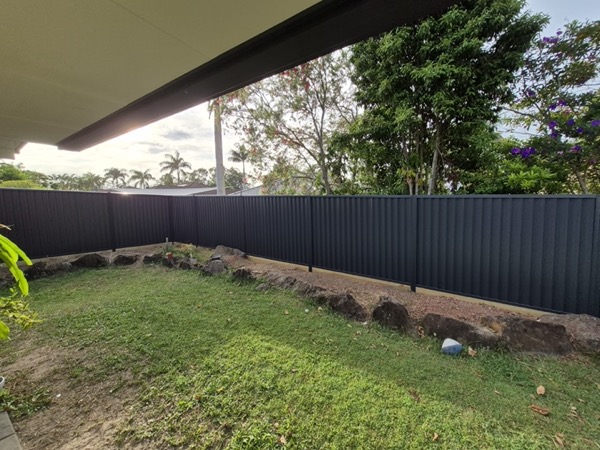 A dark Colorbond fence along a lawn under the shade of a large tree