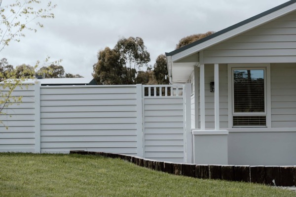 A white slatted privacy fence in front of a modern weatherboard home