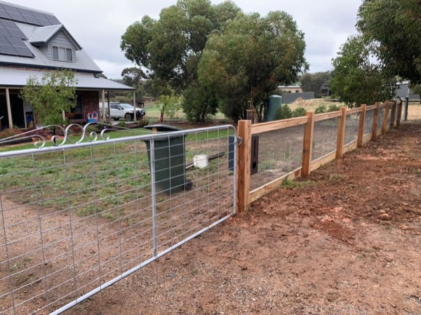A timber post and rail fence with wire infill along a rural boundary