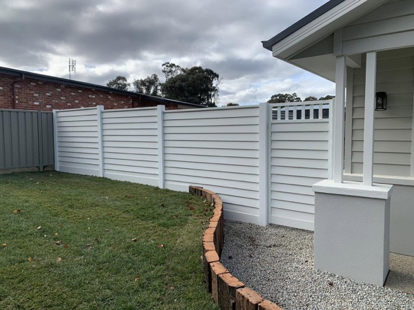 A cream Colorbond fence running past the corner of a rendered home