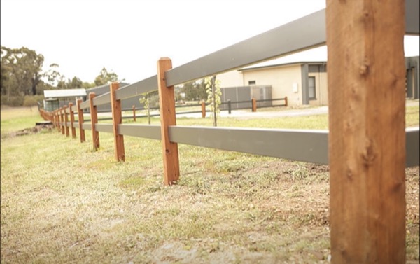 A timber post and rail fence with wire infill through a new estate