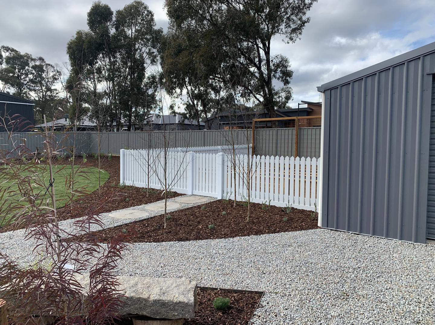 A white picket fence behind a new gravel and mulch garden bed