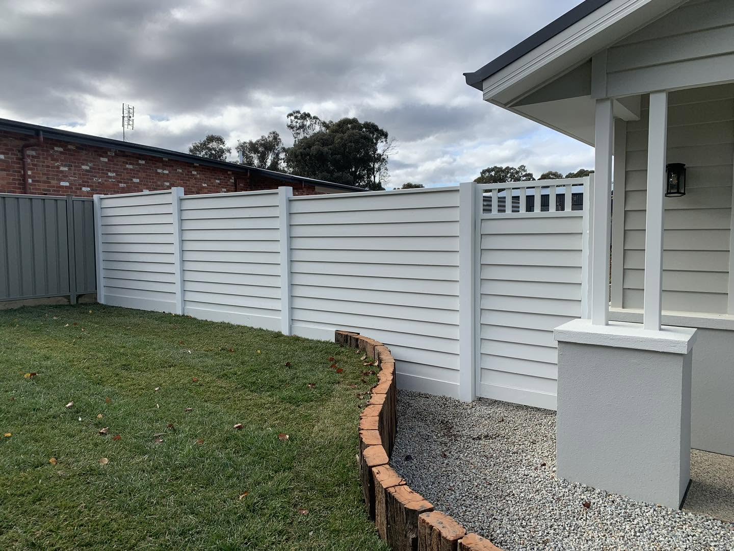 A cream Colorbond fence running past the corner of a rendered home