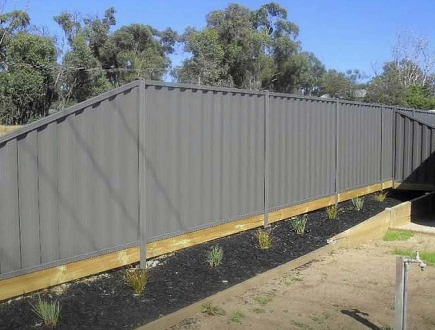 A long run of pale Colorbond fencing seen from one end